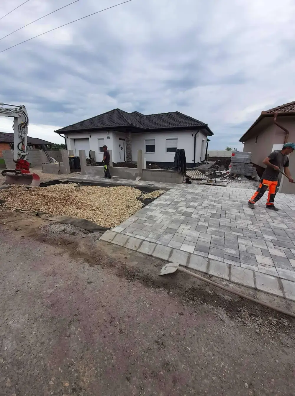 Térkövezett kocsibeálló kivitelezés közben, kotrógéppel a háttérben
