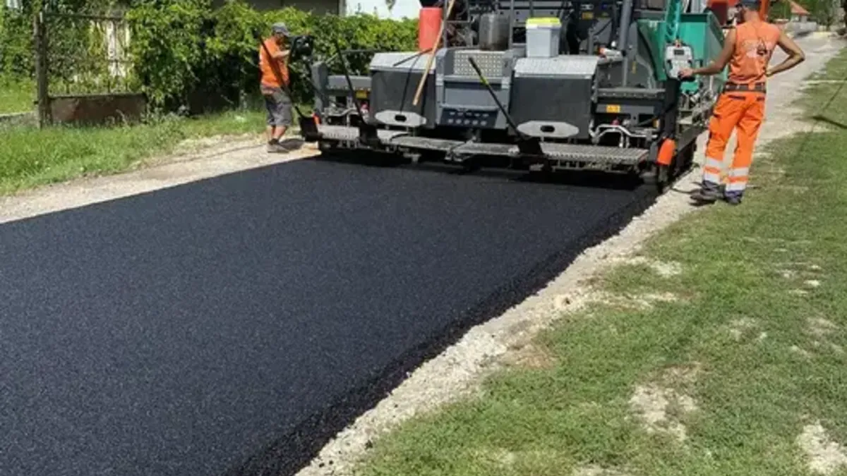 Aszfaltterítő gép meleg aszfaltot terít, mellette a kivitelező csapat