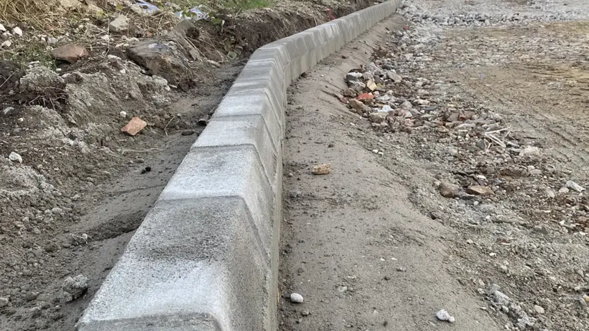 Frissen betonágyba rakott kiemelt szegély enyhe ívben, a háttérben rakodógép